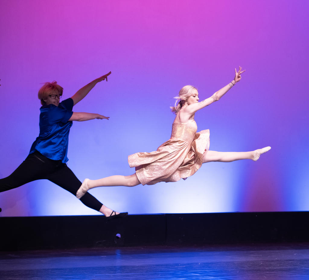 Two dance students leaping through the air during performance