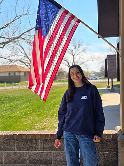 Greta Santini is the April Student Worker of the Month as is posing in front of the American flag.
